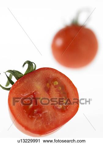 Stock Image - Half of a Tomato with a whole one in background. Fotosearch