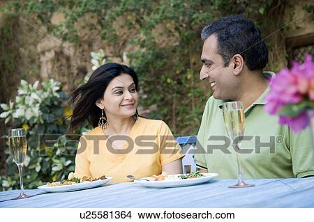 Picture - Close-up of a mid adult couple sitting at a dining table and smiling. Fotosearch
