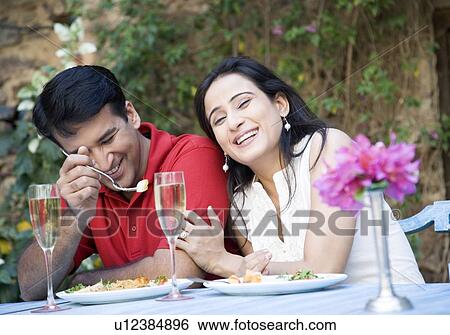 Stock Photograph - Mid adult couple sitting at a table and having food. Fotosearch