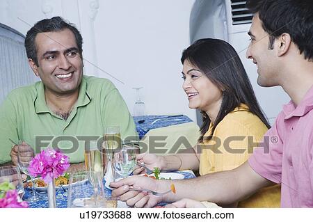 Mid adult couple sitting with a young man at a dining table View Large Photo Image Stock Photo - Mid adult couple sitting with a young man at a dining table. Fotosearch