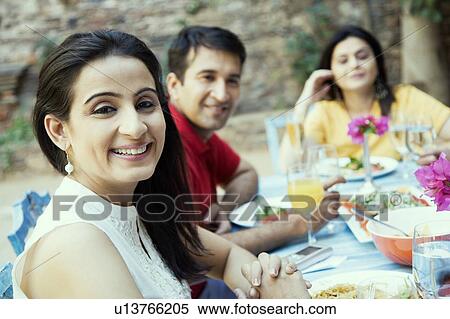 Stock Photography - Mid adult woman sitting with her friends at a dining table. Fotosearch