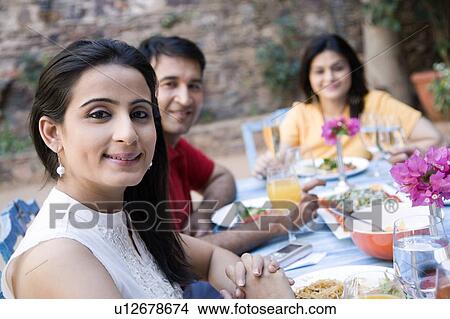 Portrait of a mid adult couple sitting with a mid adult woman at a dining table View Large Photo Image Picture - Portrait of a mid adult couple sitting with a mid adult woman at a dining table. Fotosearch