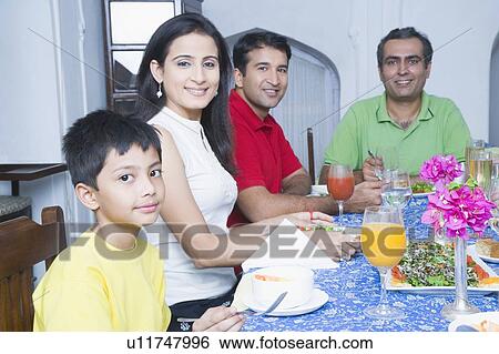 Stock Photograph - Portrait of a mid adult couple sitting with their son and a mid adult man at a dining table. Fotosearch