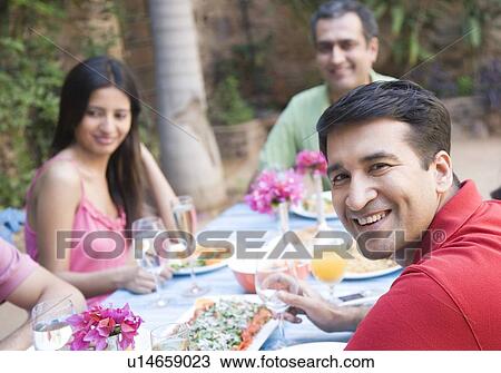 Stock Image - Portrait of a mid adult man with his friends sitting at a dining table. Fotosearch
