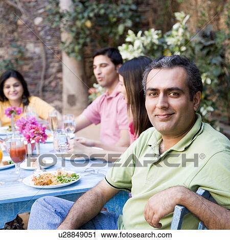 Stock Image - Portrait of a mid adult man with his friends sitting at a dining table. Fotosearch