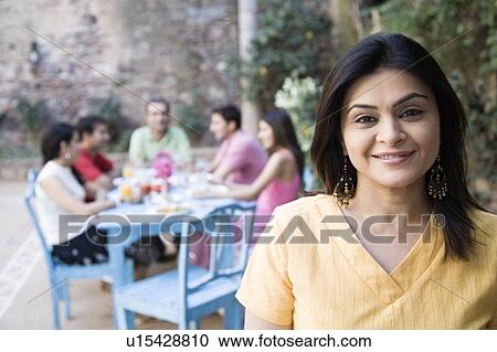 Stock Image - Portrait of a mid adult woman smiling with her friends sitting at a dining table in the background. Fotosearch