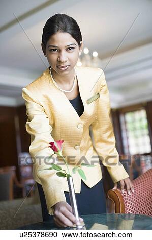 Stock Image - Portrait of a waitress putting a vase on a table in a restaurant. Fotosearch