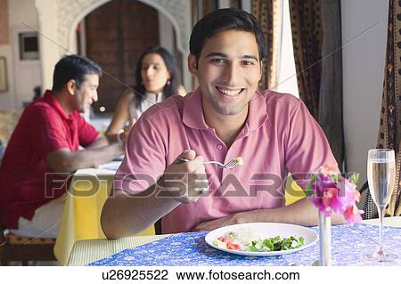 Stock Image - Portrait of a young man sitting in a restaurant and smiling. Fotosearch