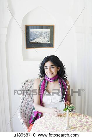 Stock Image - Portrait of a young woman sitting in a restaurant and holding a glass of lemon juice. Fotosearch