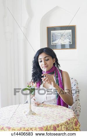 Stock Image - Young woman sitting in a restaurant and holding a glass of lemon juice. Fotosearch