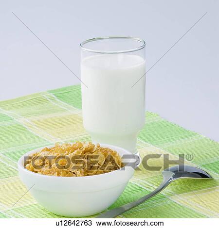 Stock Image - Close-up of a glass of milk with a bowl of corn flakes. Fotosearch