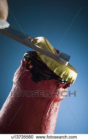 Stock Image - Close-up of a person opening a beer bottle with a bottle opener. Fotosearch