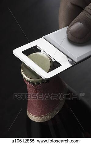 Stock Photography - Close-up of a person's hand opening a beer bottle with an opener. Fotosearch