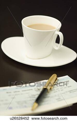 Stock Image - Close-up of a pen on a check book with a cup of tea on a saucer. Fotosearch