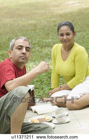 Stock Image - Mid adult couple sitting on a picnic blanket in a park . Fotosearch