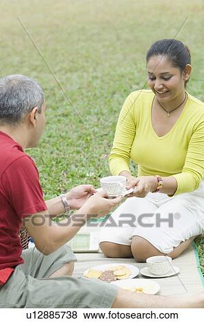 Mid adult woman giving a tea cup to a mid adult man and smiling View Large Photo Image Stock Photo - Mid adult woman giving a tea cup to a mid adult man and smiling. Fotosearch