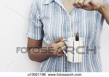 Stock Photograph - Mid section view of a woman dipping a teabag into a tea cup. Fotosearch