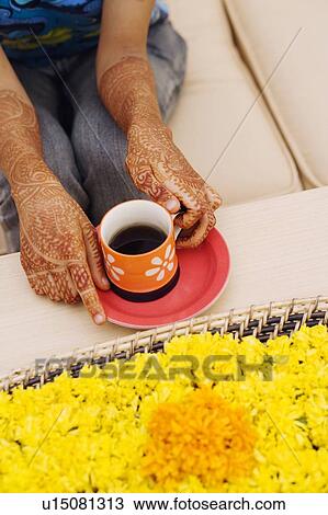 Stock Image - Mid section view of a woman holding a cup of tea in front of a tray of Marigolds. Fotosearch