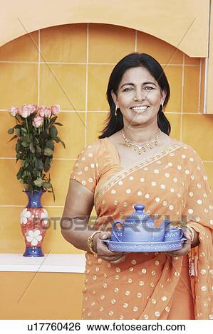Stock Photograph - Portrait of a mature woman holding tea cups and a tea kettle on a tray. Fotosearch