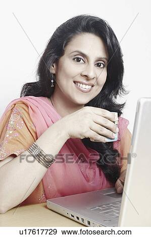 Stock Photo - Portrait of a mid adult woman holding a tea cup in front of a laptop. Fotosearch