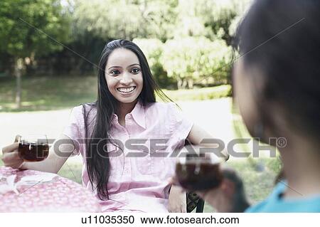 Stock Image - Teenage girl sitting with her friend holding a cup of tea. Fotosearch