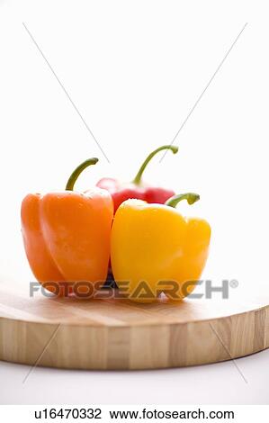 Stock Image - Yellow, orange and red peppers on butcher block cutting board in profile. Fotosearch