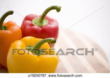 Stock Photo - Yellow, orange and red peppers on butcher block cutting board. Fotosearch
