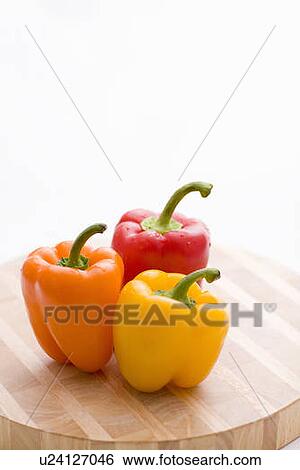 Stock Photograph - Yellow, orange and red peppers on butcher block cutting board. Fotosearch