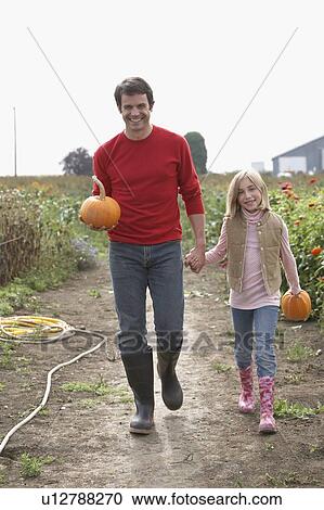 Stock Image - Father and daughter with organic pumpkins walking in farm fields, Ladner, British Columbia. Fotosearch