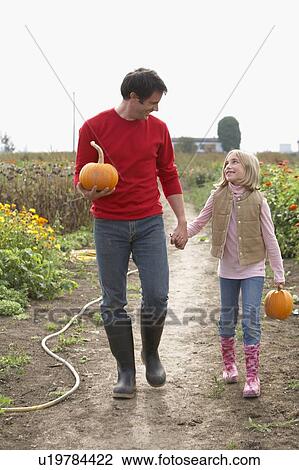 Stock Image - Father and daughter with organic pumpkins walking in farm fields, Ladner, British Columbia. Fotosearch