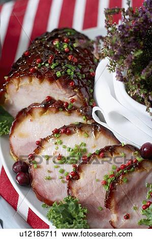 Stock Image - Festive oven roasted ham sliced and garnished with chives and cranberries. Fotosearch