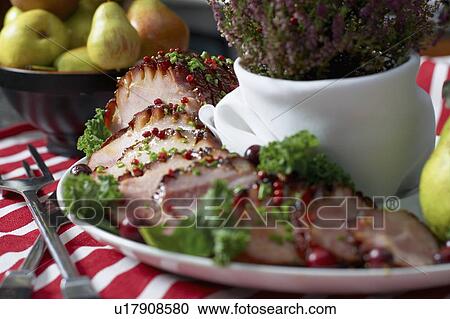 Stock Image - Festive oven roasted ham sliced and garnished with chives and cranberries accompanied by a bowl of pears and the Heather plant. Fotosearch