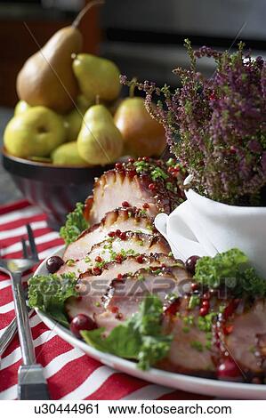 Stock Image - Festive oven roasted ham sliced and garnished with chives and cranberries accompanied by a bowl of pears and the Heather plant. Fotosearch