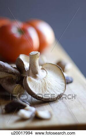 Picture - Portobello mushrooms with tomatoes on a wooden cutting board. Fotosearch