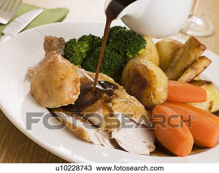 Stock Image - Gravy being Poured over a plate of Roast Chicken. Fotosearch