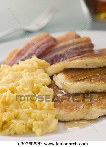 Stock Photo - American Pancakes with Crispy Bacon and Scrambled Eggs and Maple Syrup. Fotosearch