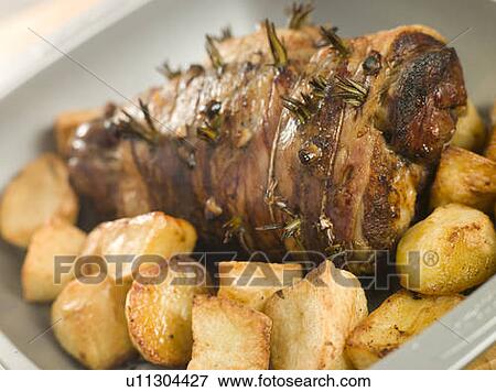 Stock Photo - Roast Leg of Lamb Studded with Garlic and Rosemary and Roast Potatoes. Fotosearch