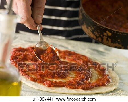 Stock Image - Spooning Tomato sauce onto a Pizza Base. Fotosearch