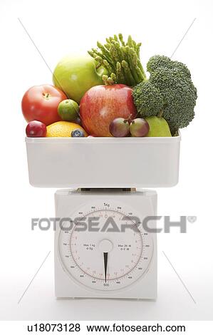 Stock Photo - A stack of fruits and vegetables on the weight scale, close-up. Fotosearch