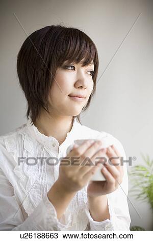 Stock Image - Young woman holding tea cup. Fotosearch