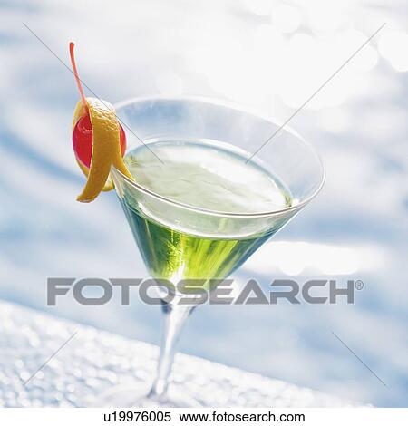 Stock Photography - Close-up of a glass of cocktail on the ledge of a swimming pool. Fotosearch