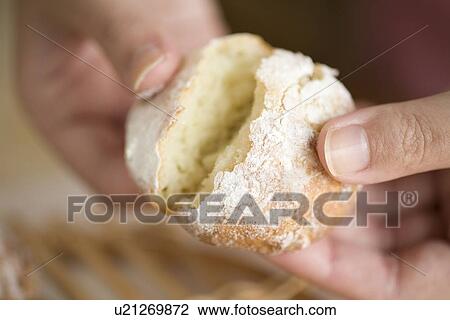 Stock Image - Human hand of young woman breaking bread fresh from oven. Fotosearch