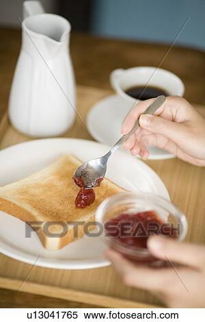 Stock Photography - Human hand of young woman spreading jam on toast. Fotosearch