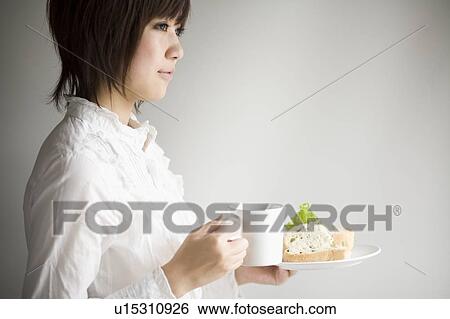 Stock Photograph - Young woman holding sandwiches plate and coffee cup. Fotosearch