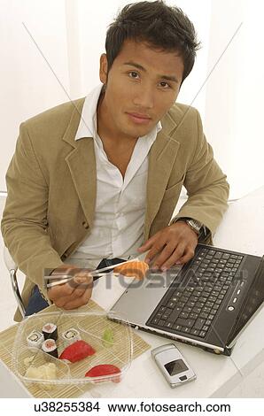 Picture - Asian man is eating sushi on his desk. Fotosearch