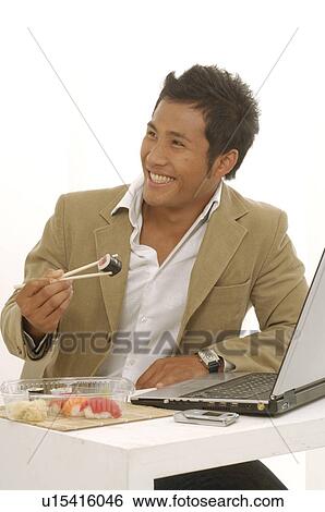 Asian man is eating sushi on his desk View Large Photo Image Stock Photograph - Asian man is eating sushi on his desk. Fotosearch