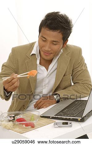 Stock Photograph - Asian man is eating sushi on his desk. Fotosearch