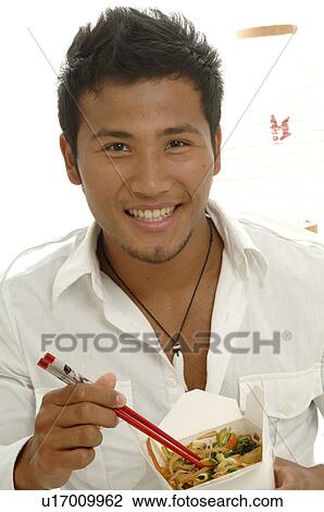 Stock Image - Man is eating an Asian meal in a lunch box with chopsticks. Fotosearch