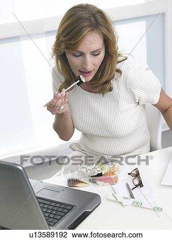 Stock Image - Woman is eating sushi at the desk. Fotosearch