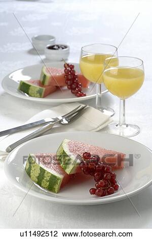 Stock Image - Place setting with melon, red currant and juice. Fotosearch